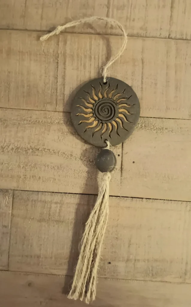 Suspension décorative artisanale en grès noir, motif soleil dorée, pompon en ficelle de jute, Isabelle Morales